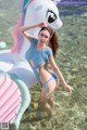 A woman in a blue swimsuit standing in the water next to a unicorn float.