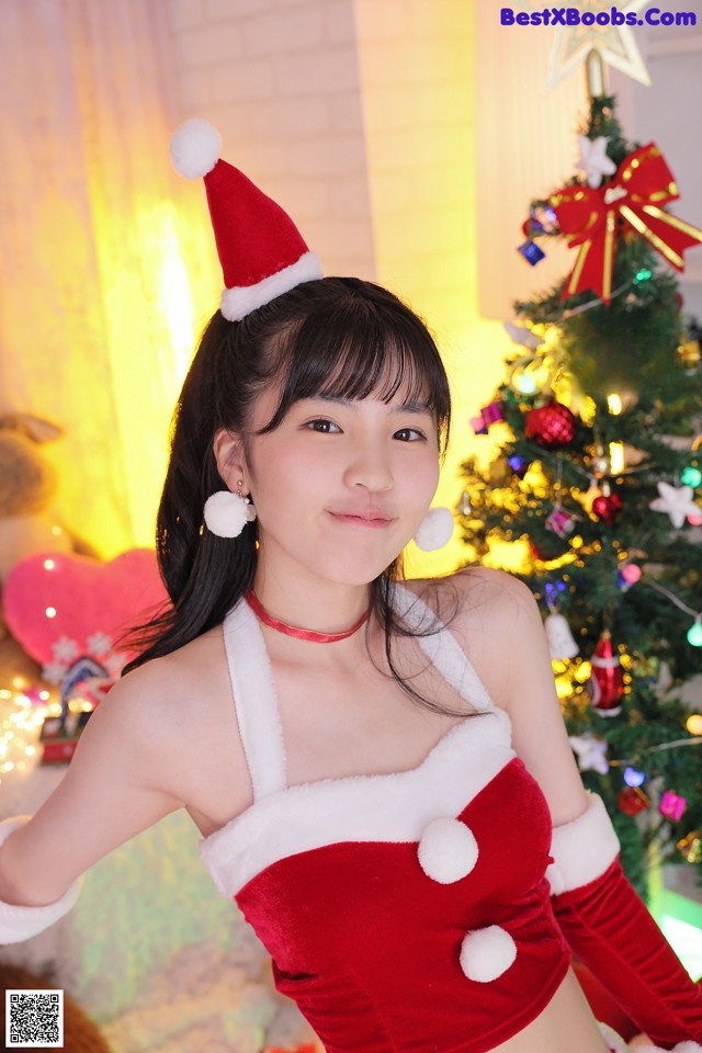 A woman in a santa outfit posing in front of a Christmas tree.