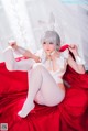 A woman in a white bunny costume sitting on a red bed.