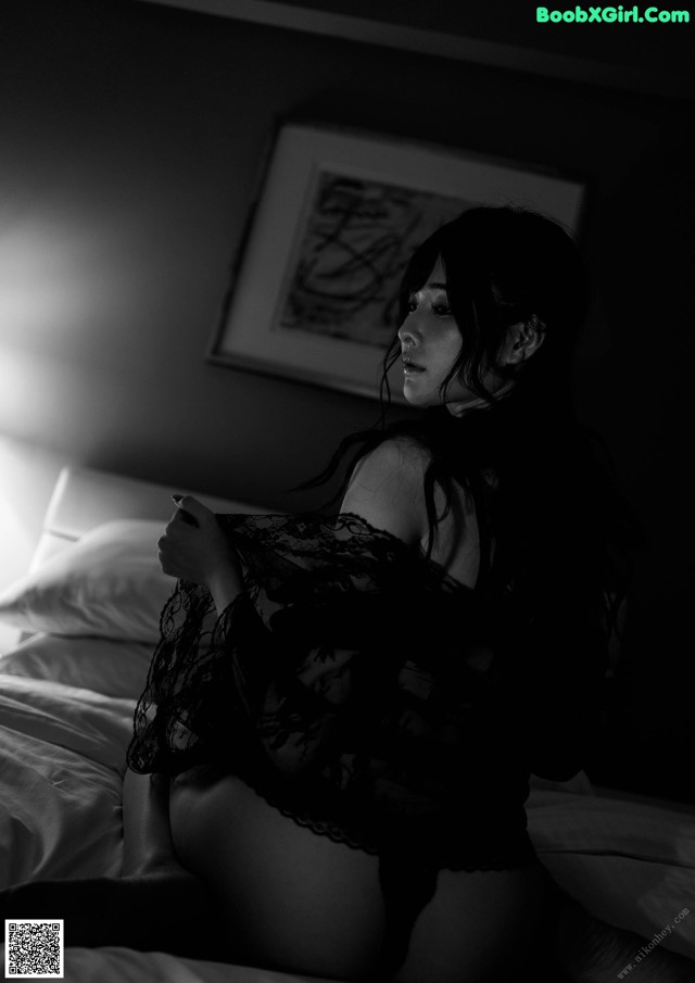 A woman sitting on a bed in a black and white photo.
