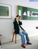 A woman sitting on a stool in front of a painting.