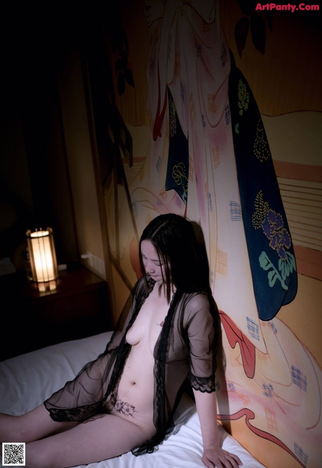 A naked woman sitting on a bed in a room.