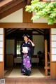 A woman in a kimono standing in a doorway holding a book.